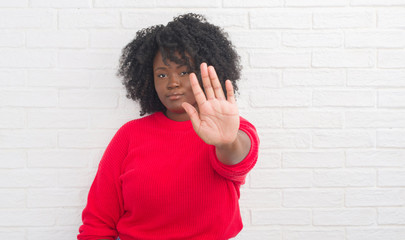 Young african american plus size woman over white brick wall doing stop sing with palm of the hand....