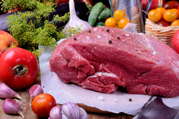 Big piece of beef meat sprinkled with spices. Vegetables and herbs around