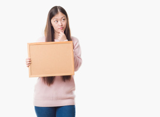 Young Chinese woman over isolated background holding corkboard serious face thinking about question, very confused idea