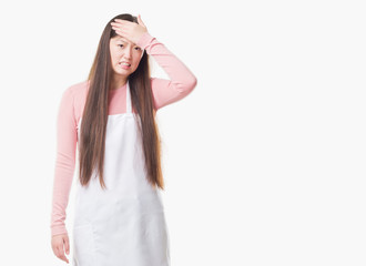 Fototapeta premium Young Chinese shop owner woman over isolated background wearing white apron stressed with hand on head, shocked with shame and surprise face, angry and frustrated. Fear and upset for mistake.