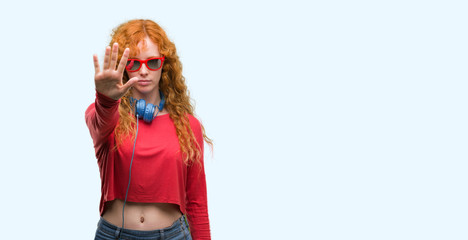 Young redhead woman wearing headphones with open hand doing stop sign with serious and confident...
