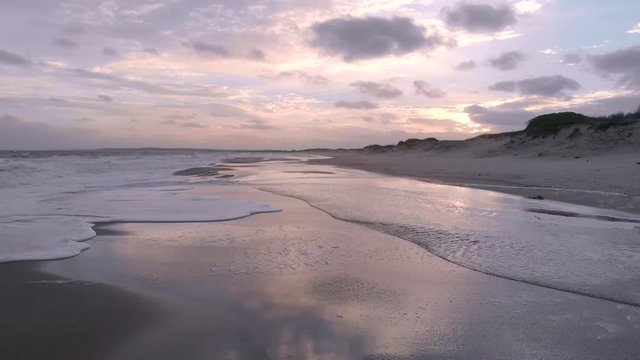 Low and fast aerial shot moving backwards looking at sunset with reflecion on water over gentle waves