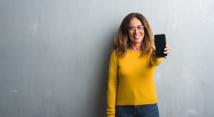 Middle age hispanic woman showing smarphone screen with a happy face standing and smiling with a...