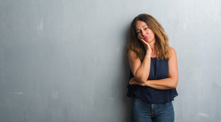 Middle age hispanic woman standing over grey grunge wall thinking looking tired and bored with depression problems with crossed arms.
