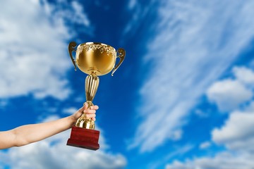 Hand holding golden trophy on sky background
