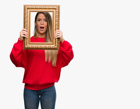 Beautiful young woman holding vintage frame scared in shock with a surprise face, afraid and excited with fear expression