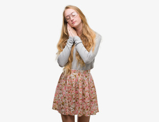Blonde teenager woman wearing flowers skirt sleeping tired dreaming and posing with hands together while smiling with closed eyes.