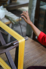 Closeup of traditional wooden spinning wheel used for making silk thread with woman's hand. Vertical view.
