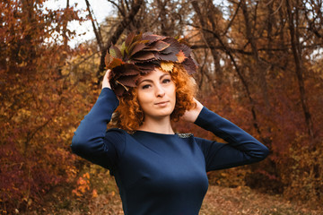 Redhead curly girl holding a wreath of grape leaves in a blue dress. Young witch in the wood.