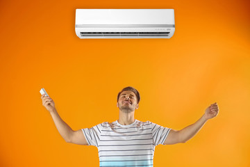 Happy young man with air conditioner remote on color background