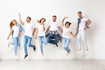 Group of young people in jeans jumping near light wall