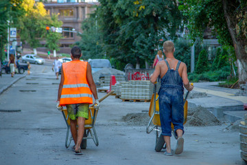 Workers with building wheelbarrows work on the construction of sidewalk. Workers are carrying empty construction wheelbarrows to load construction materials. Workers transport building materials.