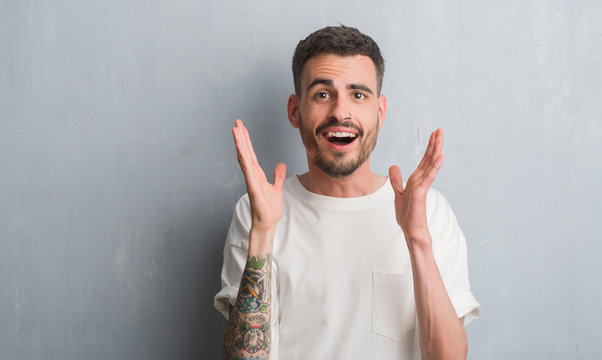 Young adult man standing over grey grunge wall very happy and excited, winner expression celebrating victory screaming with big smile and raised hands