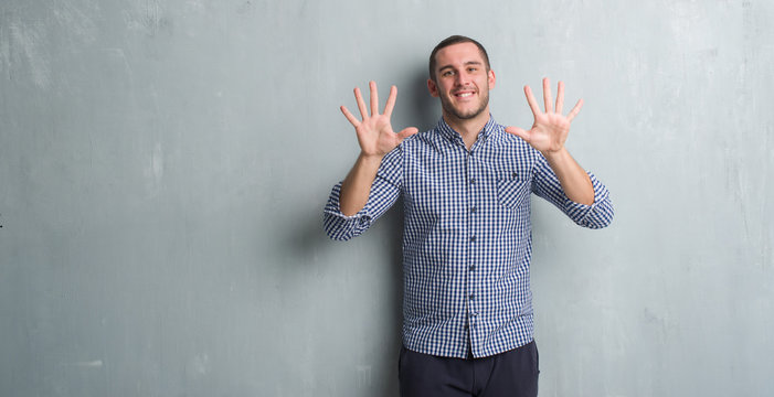 Young caucasian man over grey grunge wall showing and pointing up with fingers number ten while smiling confident and happy.