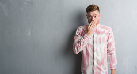 Young redhead man over grey grunge wall cover mouth with hand shocked with shame for mistake, expression of fear, scared in silence, secret concept