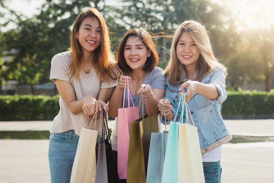 Group of young Asian woman shopping in an outdoor market with shopping bags in their hands. Young Asian women show what they got in shopping bag under warm sunlight. Group outdoor shopping concept.