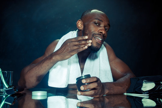 The young african man in bedroom sitting in front of the mirror after scratching his beard at home. Human emotions concept. after shave cream concepts
