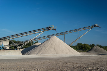 Conveyor over heaps of gravel on blue sky at an industrial cement plant.