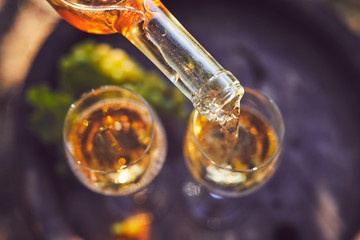Pouring white wine into glasses on a wooden barrel, top view