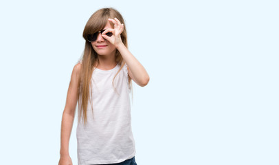 Obraz premium Young blonde toddler wearing sunglasses with happy face smiling doing ok sign with hand on eye looking through fingers