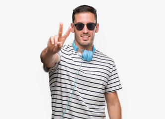 Naklejka premium Handsome young man wearing headphones smiling looking to the camera showing fingers doing victory sign. Number two.
