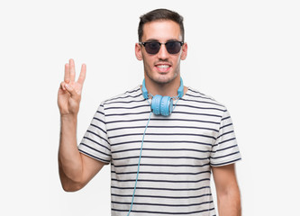 Handsome young man wearing headphones showing and pointing up with fingers number three while smiling confident and happy.
