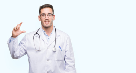 Fototapeta premium Handsome young doctor man smiling and confident gesturing with hand doing size sign with fingers while looking and the camera. Measure concept.