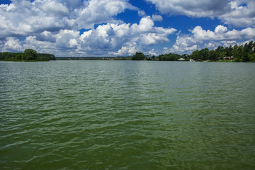 A beautiful image of landscape from the center of the river, surrounded by trees and reeds on the shore and distant horizon against the blue sky in clouds. Reflection, water, tourist destination