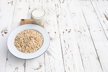 Oatmeal, rolled oats on white wooden background wilt glass of milk. Porridge oats flakes