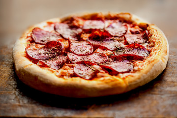 Hot pizza with Pepperoni, melting cheese on a rustic wooden table closeup.  Pizza Ready to Eat.