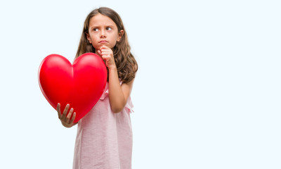 Fototapeta na wymiar Brunette hispanic girl holding red heart serious face thinking about question, very confused idea