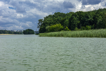 A beautiful image of landscape from the center of the river, surrounded by trees and reeds on the shore and distant horizon against the blue sky in clouds. Reflection, water, tourist destination