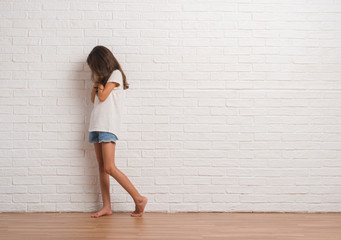 Young hispanic kid stading over white brick wall with sad expression covering face with hands while...