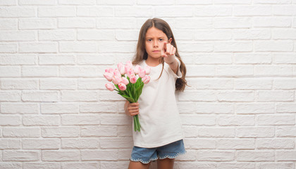 Young hispanic kid over white brick wall holding flowers on mother day pointing with finger to the camera and to you, hand sign, positive and confident gesture from the front