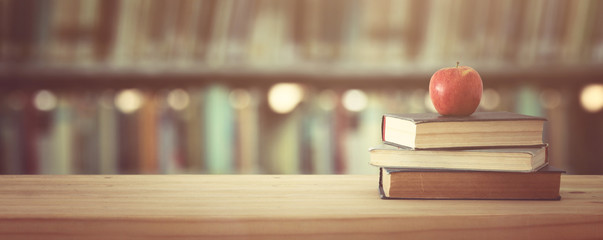 back to school concept. stack of books over wooden desk in front of library.