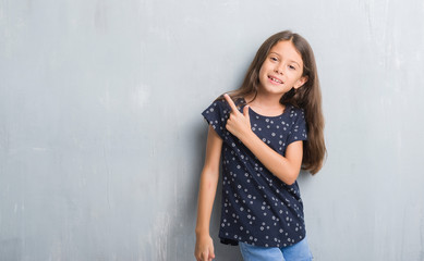 Young hispanic kid over grunge grey wall cheerful with a smile of face pointing with hand and finger up to the side with happy and natural expression on face looking at the camera.