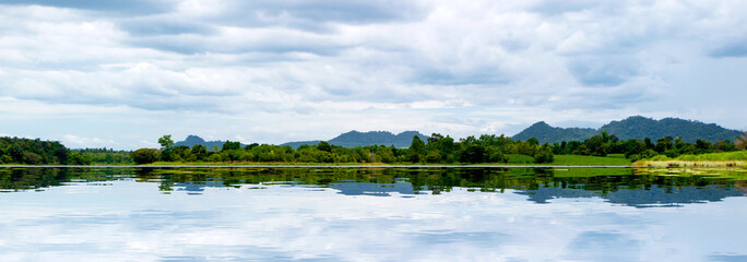Panorama landscape view of nature in Thailand, reflection of forrest in lake. Mountain and blue sky in background in summer season