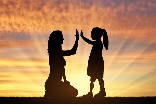 Disabled baby girl with prosthetic legs with her mom outdoors at sunset.
