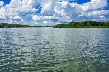 A beautiful image of landscape from the center of the river, surrounded by trees and reeds on the shore and distant horizon against the blue sky in clouds. Reflection, water, tourist destination
