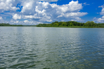 A beautiful image of landscape from the center of the river, surrounded by trees and reeds on the shore and distant horizon against the blue sky in clouds. Reflection, water, tourist destination