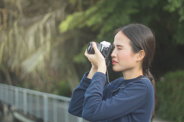 pretty cool young Asian woman with retro film camera or mirrorless camera in modern garden park