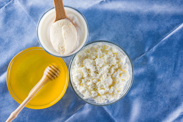 Dairy products and honey with wooden cutlery. Cottage cheese, sour cream, cream on a blue napkin top view. Different natural products for vegan. Healthy food. Copy space