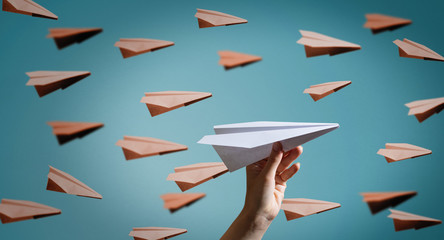 Hand launches a paper plane to towards other aircrafts on blue background