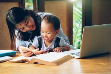 Business woman teaching her child about investment with multimedia and book, home school education.