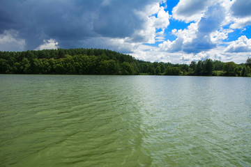 A beautiful image of landscape from the center of the river, surrounded by trees and reeds on the shore and distant horizon against the blue sky in clouds. Reflection, water, tourist destination