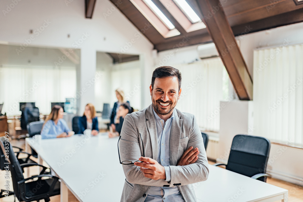 Wall mural portrait of a smiling handsome businessman with crossed arms in a meeting room.