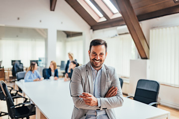 Fototapeta premium Portrait of a smiling handsome businessman with crossed arms in a meeting room.