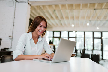 Beautiful woman with a toothy smile working on a laptop in modern office.