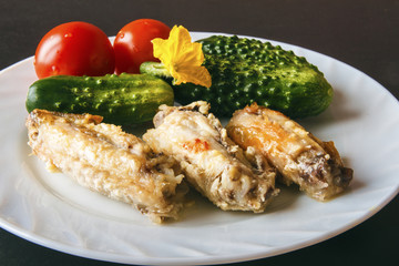 Baked poultry chicken wings, fresh tomatoes and green cucumbers on a white plate on a black background. Healthy healthy food for dinner or lunch