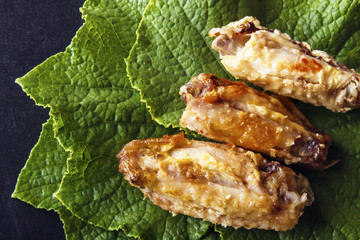 Baked crispy chicken wings on green cucumber leaves on a black background. Top view from above. Copy space for text